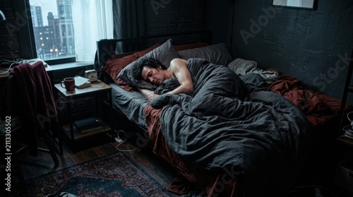 Man Sleeping Peacefully Under Duvet In Dark Bedroom With City View