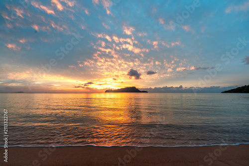Beautiful sunset over the ocean with orange colour clouds and view on small island