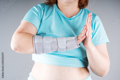 Unrecognizable woman wearing wrist orthopedic brace for carpal tunnel syndrome, sprain and joint pain rehabilitation. Gray medical splint
