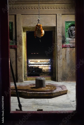 Fotografía Ancient Shiva lingam inside riverside temple with illuminated boat beyond