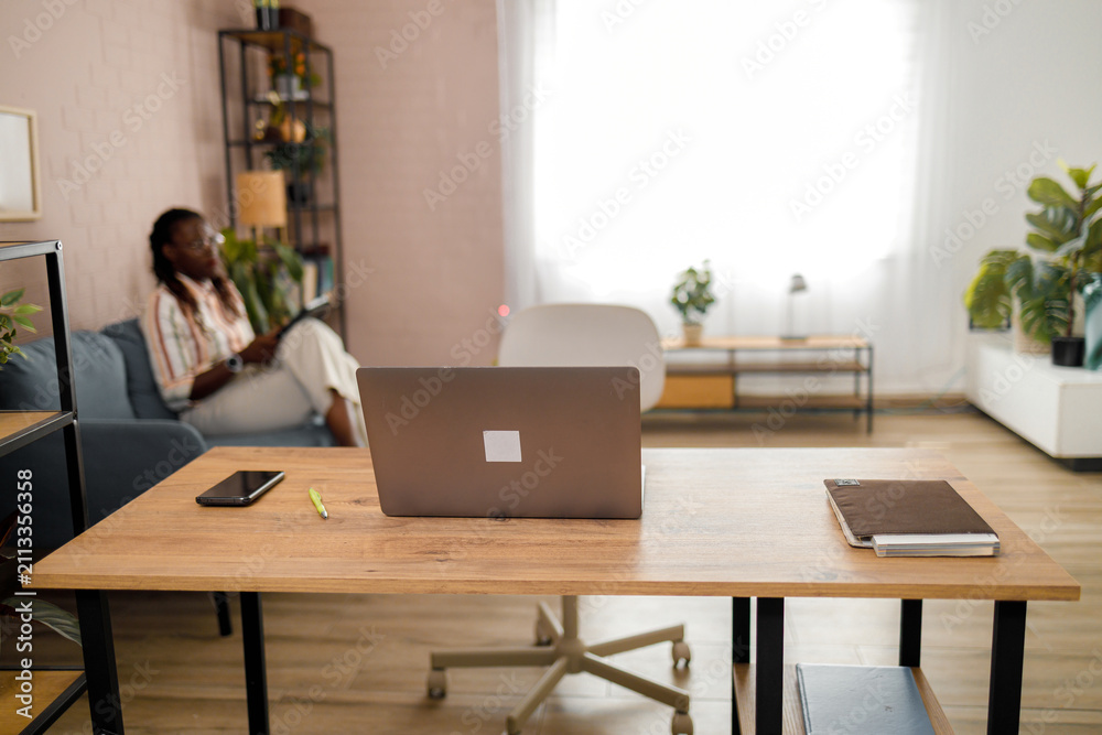 Fototapeta premium Workspace with a desk, laptop, and person relaxing in a living room