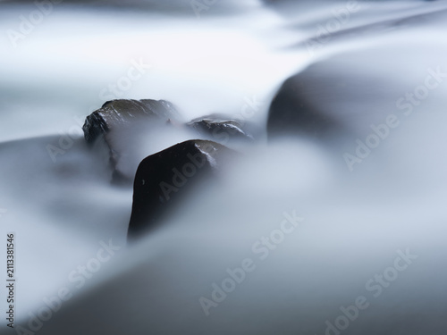 Long-exposure photographs of flowing water show dark, wet rocks partially submerged, creating a soft, misty or veiled effect around the rocks.