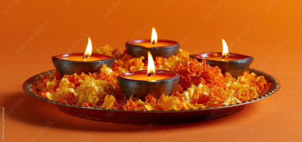 Obraz premium Glowing Indian lamps with marigold petals on orange background celebrating Diwali festival ambiance.