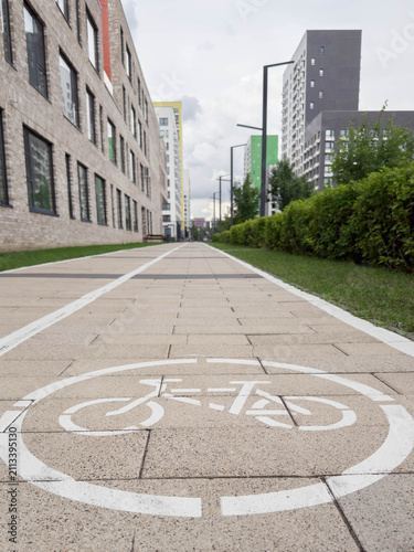 Dedicated bicycle lane with pavement marking stretching between modern residential buildings, green landscaping, clean urban environment, promoting sustainable mobility, city transportation concept