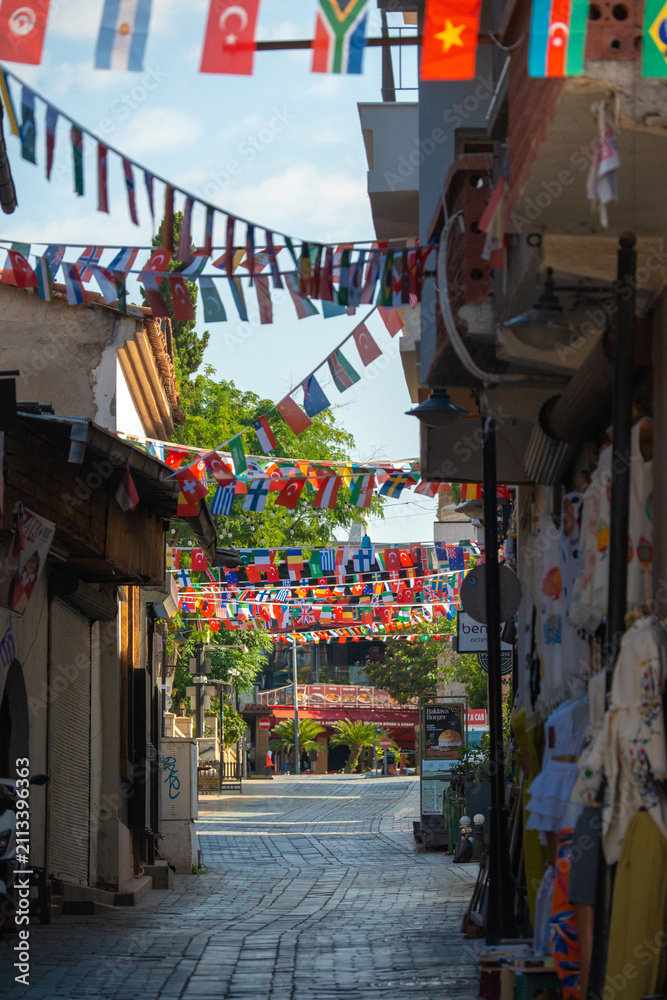Fototapeta premium Narrow tourist street decorated with international flags in Kaleici old town Antalya Turkey