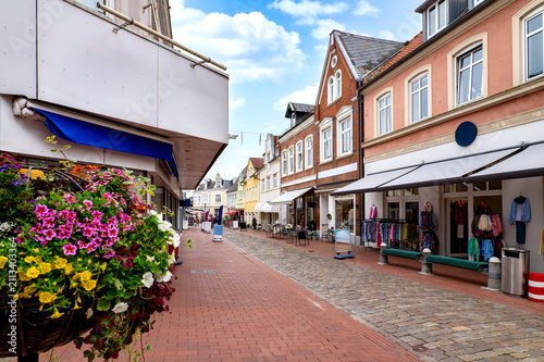 Shopping street in Kappeln featuring retail stores, colorful flower displays, historic buildings and a pedestrian street beneath a blue sky.. Germany