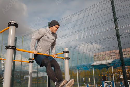 Fotografie Athletic young man doing parallel bar dips during street workout at outdoor spor