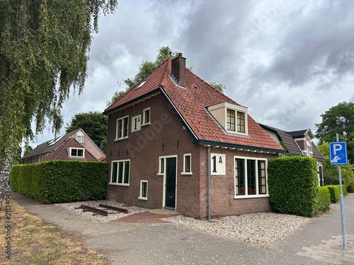 Foto Historic Dutch railway crossing keeper house 1A along the former Koningslijn railway line on Asselsestraat in Apeldoorn, featuring original brickwork and train track piece