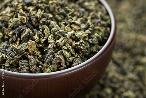 Dark wood bowl overflowing with Tie Guan Yin on full tea background