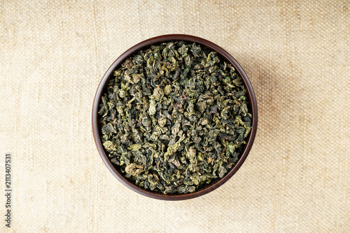 Overhead macro of green oolong in wooden cup on light burlap