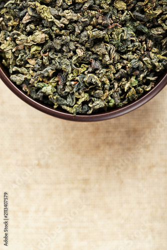 Top view closeup dark wood cup full of loose tea on natural fabric