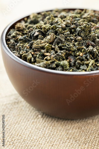 Top view closeup dark wood cup full of loose tea on natural fabric