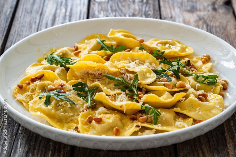 Obraz premium Cooked ravioli with pine nuts, rocket leaves and grated parmesan cheese on wooden table