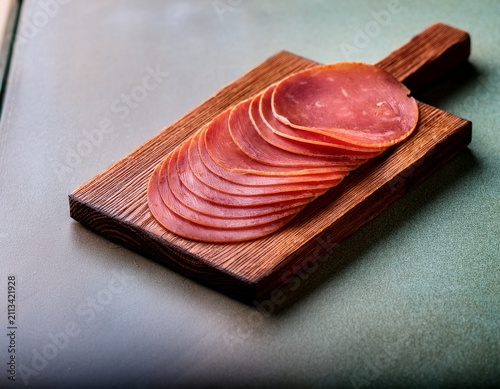 a close up photograph of thinly sliced red meat likely ham or salami arranged on a wooden cutting board