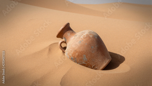 weathered clay wine jar half-buried in ancient desert sand dunes