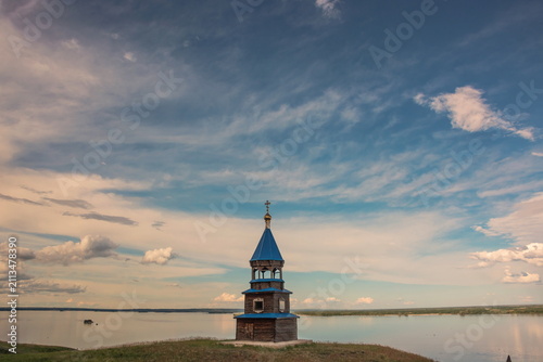 Evening landscape with wooden chapel on the background of sky and river
