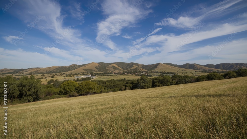 Obraz premium Expansive landscape with grassy fields, rolling hills, and a bright blue sky with clouds.