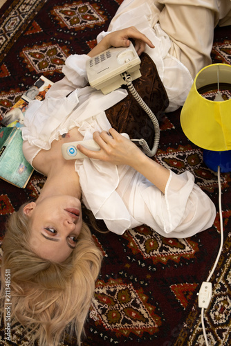Obraz na płótnie Young woman lying on a patterned vintage rug while holding a retro rotary telephone