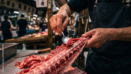 Japanese fishmonger scraping leftover red tuna meat from a fish backbone using a spoon at a busy fish market, preparing nakaochi