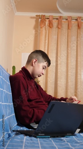 Teenager is sitting on a couch, continuously working with a laptop and tablet, drawing, writing or copying study material at home.