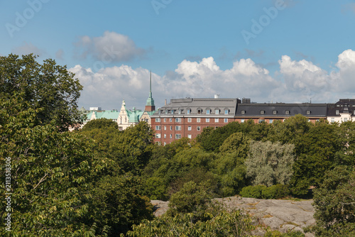 HELSINKI, FINLAND - AUGUST 14, 2025: A red-brick institutional building with a green-domed tower stands among trees as seen from an elevated granite outcrop.