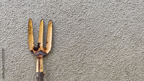 Quadro su tela A close-up shot of an old, used hand garden fork with worn metal tines placed against a textured grey concrete wall