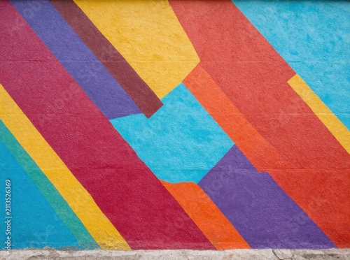 Vibrant abstract geometric mural with bold diagonal stripes and colorful block shapes on textured wall, modern retro pop art street background concept
