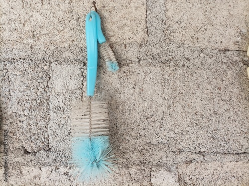 Foto Blue bottle cleaning brush hanging on a rough concrete wall.