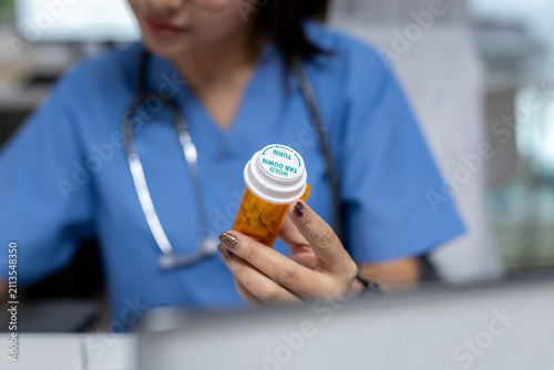 healthcare professional in blue medical scrubs examining prescription medicine bottle in clinic. Focus on medication safety, pharmaceutical care, patient treatment, and healthcare services.