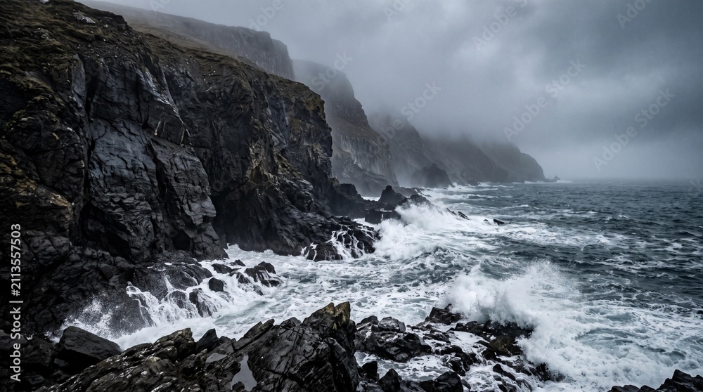 Obraz premium Dramatic coastal landscape featuring rugged cliffs and crashing waves under a moody sky with dark clouds and mist over the ocean in a remote area