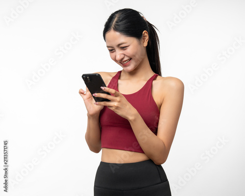 Young beautiful asian woman with red sportswear using smartphone on isolated white background. Attractive Portrait latin sporty woman standing pose holding cell phone exercise workout in studio.