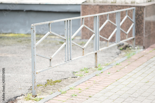 Metal pedestrian guardrail barrier dividing paved sidewalk and asphalt road in urban environment.