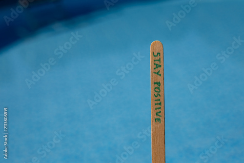 Quadro su tela Woman holding a popsicle stick with the words Stay positive against a blue swimming pool background, creating an uplifting summer lifestyle concept about optimism, happiness and positive thinking