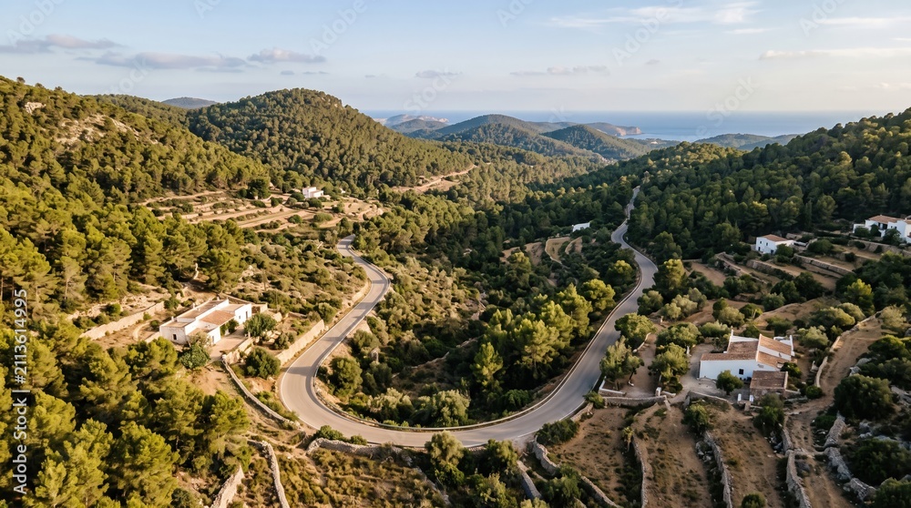 Obraz premium Aerial view of a winding asphalt road through the lush green hills of Ibiza, featuring traditional white Mediterranean houses and sea views in a summer travel concept.