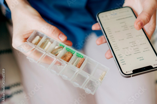 Close-up cropped view of a vitamin pill organizer and mobile phone in the hands of a woman.