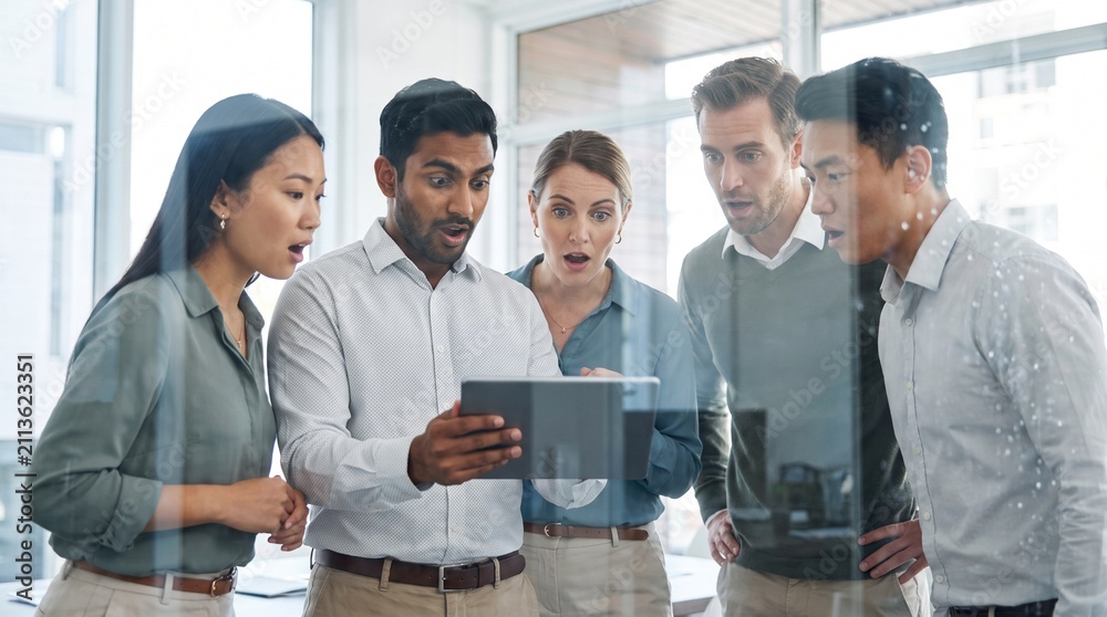 Fototapeta premium Group of diverse multi-ethnic business professionals expressing shock and amazement while looking at a digital tablet in a modern office.
