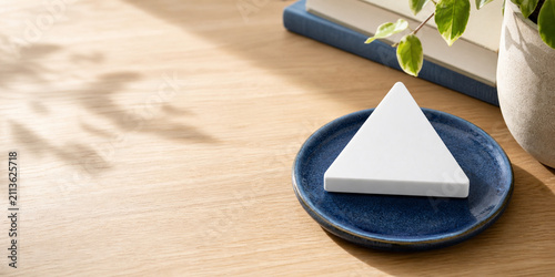 White equilateral triangle paperweight on blue ceramic coaster, neutral still life for editorial header