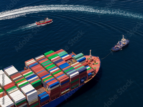 Container ship navigating port waters with tugboat assistance