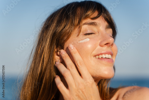 Smiling woman applies sunscreen on her cheekbones