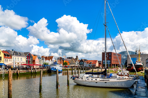 Obraz na plátně Sailing yacht in the harbor of Husum with the historic old town, waterfront promenade and dramatic clouds beneath a blue sky
