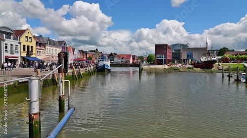 Harbor of Husum with the historic old town, waterfront promenade and dramatic clouds beneath a blue sky.
