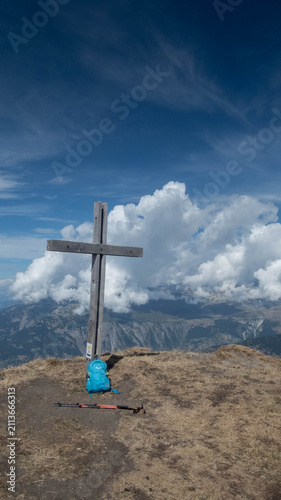 A majestic, weathered wooden summit cross stands prominently on a grassy mountain peak  Folluhorn in the Swiss Alps