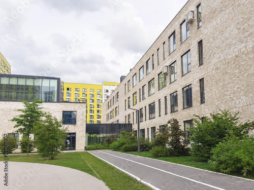 Modern school building with contemporary brick architecture, landscaped campus, pedestrian pathway, green courtyard, cloudy sky, reflecting education, innovation, sustainable learning