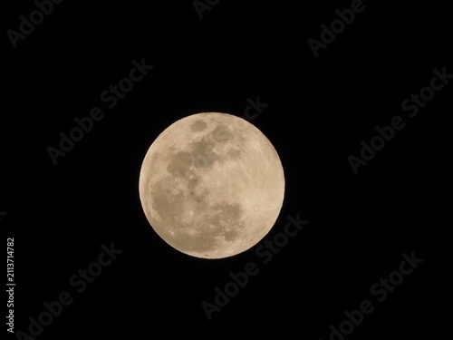 Full moon glowing warmly against a pitch black night sky, showing visible surface craters and detailed lunar geography.