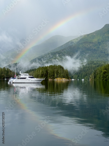 Rainbow reflected in tranquil bay over a yacht