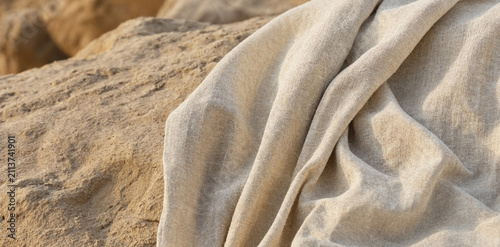 Soft beige fabric draped on rough textured rock with material background minimalist backdrop contrast interior homespun structure composition close-up