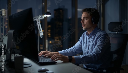 Man Working on Computer at Night in a Modern Office With City Lights in the B...