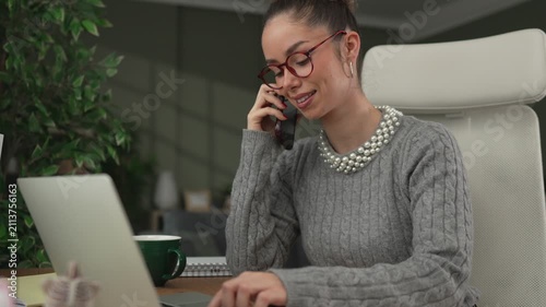 Businesswoman talking on phone while working on laptop in the office