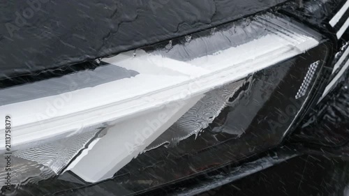 Water flows across a black car surface during washing, creating clean reflections and droplets while illustrating professional automotive detailing, maintenance, rinsing, and exterior care.
