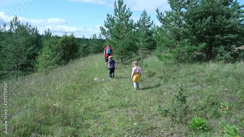 Father walking with his two little children in summer forest. Dad hiking with son and daughter on green grass field, weekend outdoor adventure activity theme. Active Family Lifestyle. Nature Escape